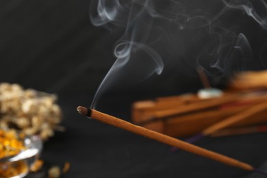 Photo of Aromatic incense stick smoldering on black table, closeup