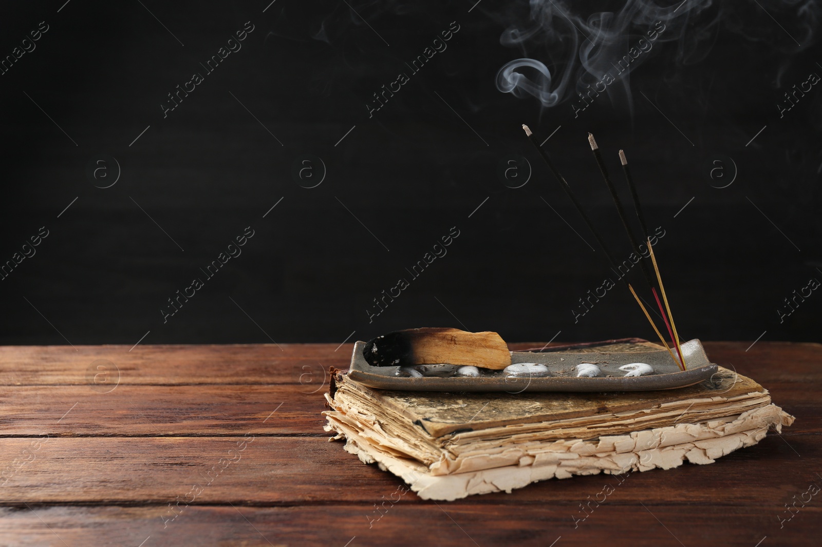 Photo of Aromatic incense sticks smoldering on wooden table. Space for text