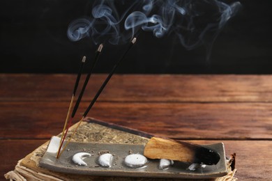 Photo of Aromatic incense sticks smoldering on wooden table, closeup. Space for text