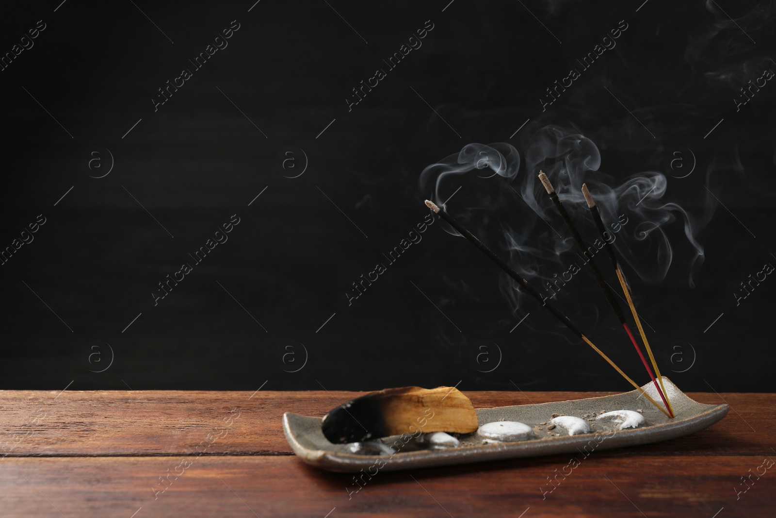 Photo of Aromatic incense sticks smoldering on wooden table. Space for text