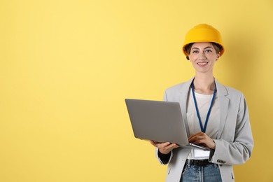 Engineer in hard hat with laptop on yellow background, space for text