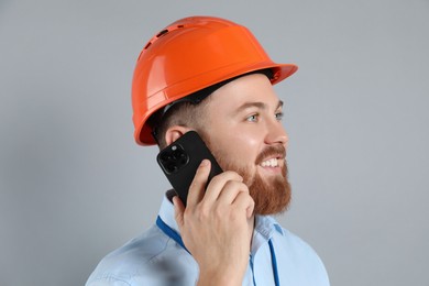 Photo of Engineer in hard hat talking on smartphone against grey background