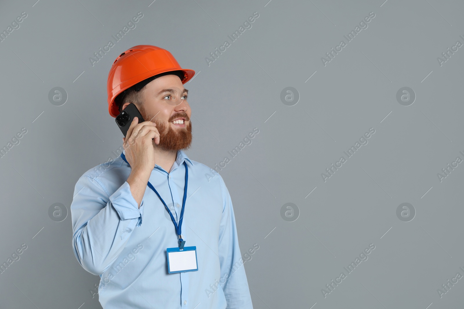 Photo of Engineer in hard hat talking on smartphone against grey background, space for text