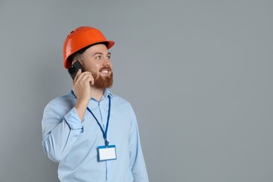 Engineer in hard hat talking on smartphone against grey background, space for text