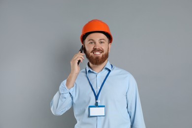 Photo of Engineer in hard hat talking on smartphone against grey background