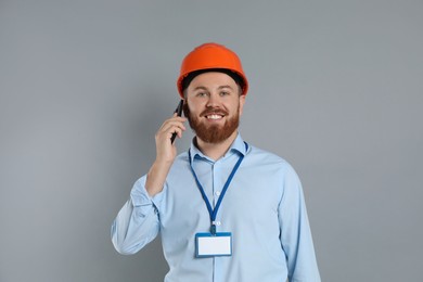 Engineer in hard hat talking on smartphone against grey background