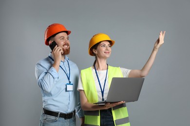 Photo of Engineer talking on smartphone while his colleague holding laptop against grey background