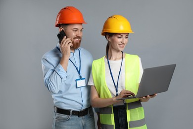 Photo of Engineer talking on smartphone while his colleague holding laptop against grey background