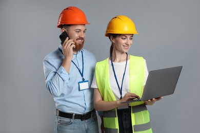 Engineer talking on smartphone while his colleague holding laptop against grey background