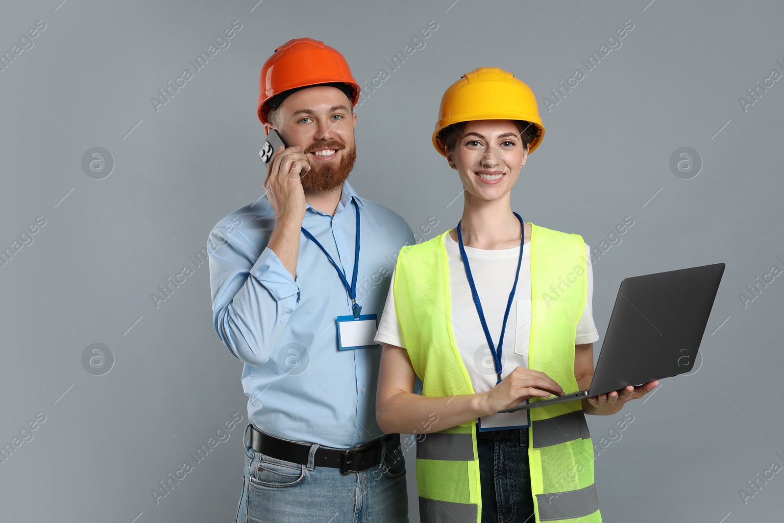 Photo of Engineer talking on smartphone while his colleague holding laptop against grey background