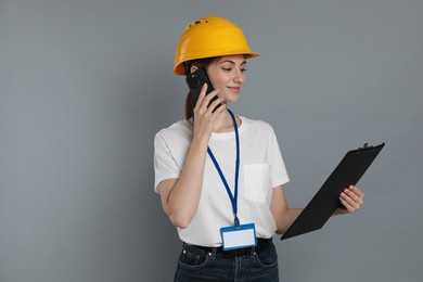 Photo of Engineer in hard hat with clipboard talking on smartphone against grey background, space for text