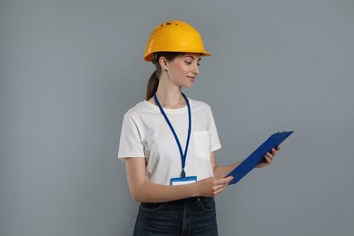 Engineer in hard hat with clipboard on grey background