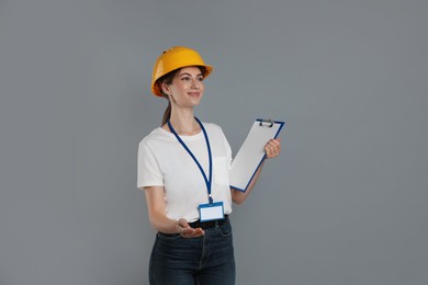 Engineer in hard hat with clipboard on grey background