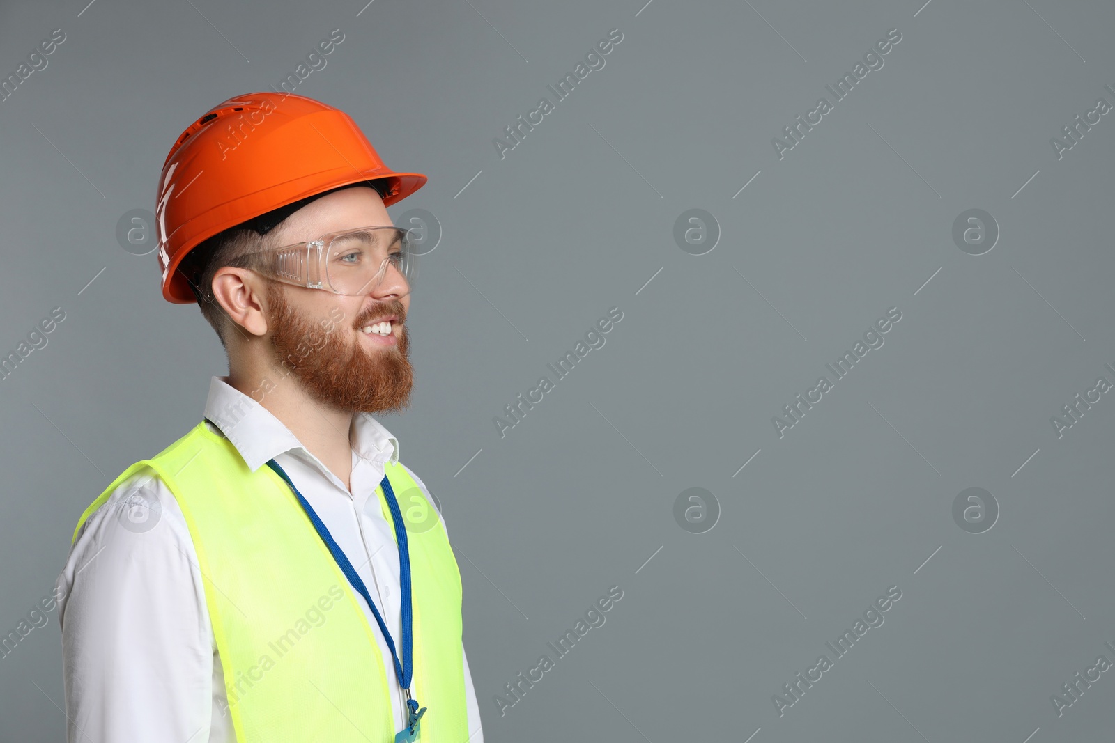 Photo of Engineer in hard hat and goggles on grey background, space for text