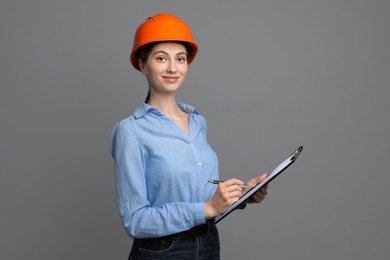 Photo of Engineer in hard hat with clipboard and pen on grey background