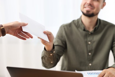 Photo of Smiling employee receiving envelope with salary from boss in office, closeup