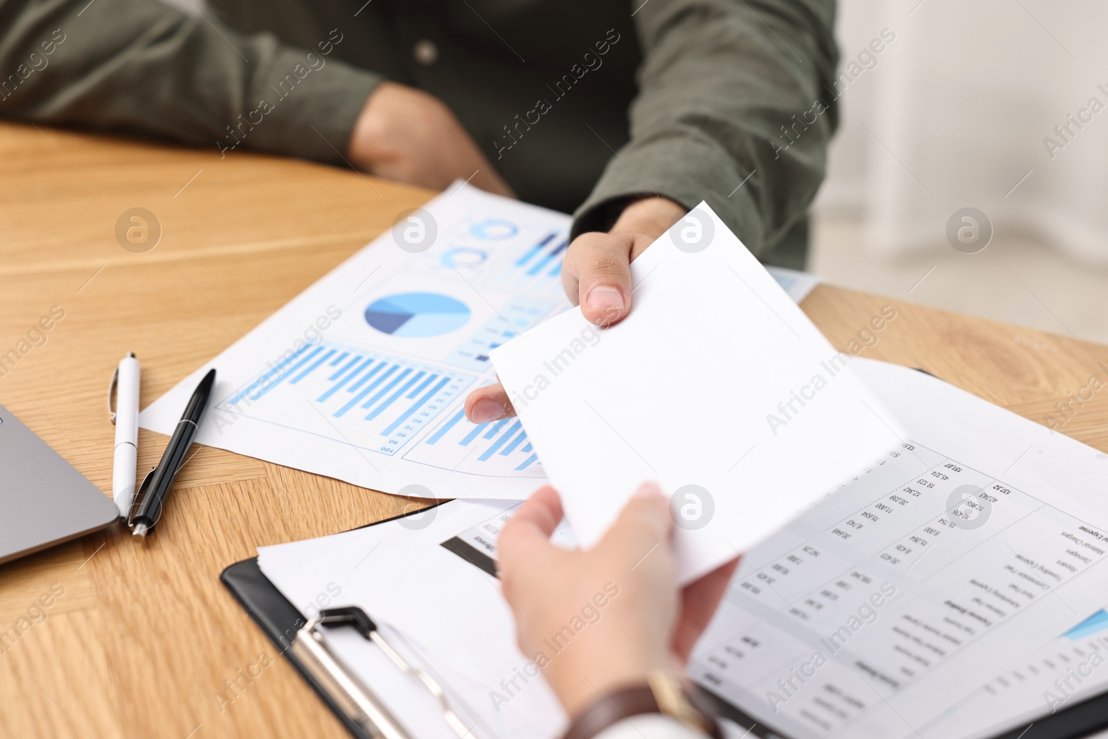 Photo of Employee receiving envelope with salary from boss at wooden table, closeup