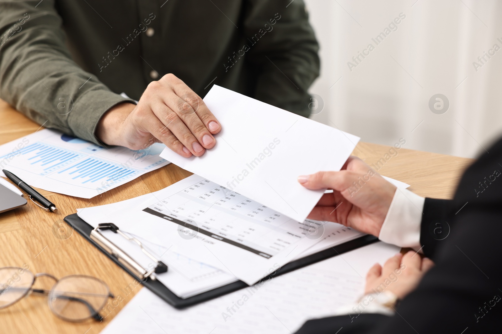 Photo of Employee receiving envelope with salary from boss at wooden table, closeup