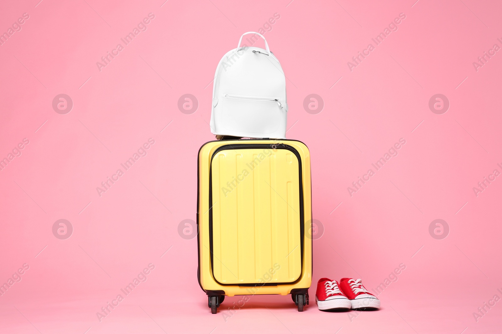 Photo of Yellow suitcase, sneakers and backpack on pink background