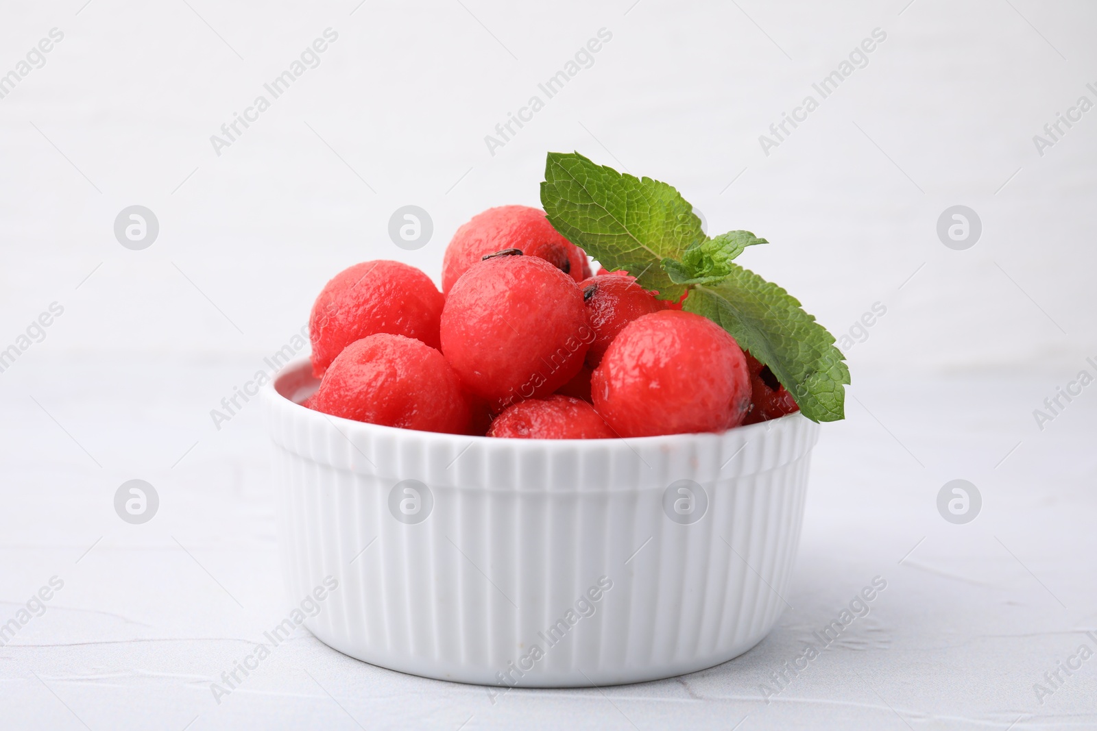 Photo of Tasty watermelon balls with mint in bowl on white table