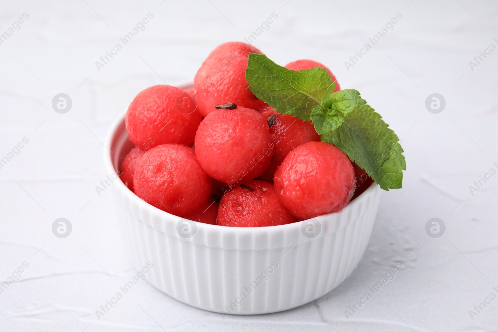 Photo of Tasty watermelon balls with mint in bowl on white table, closeup