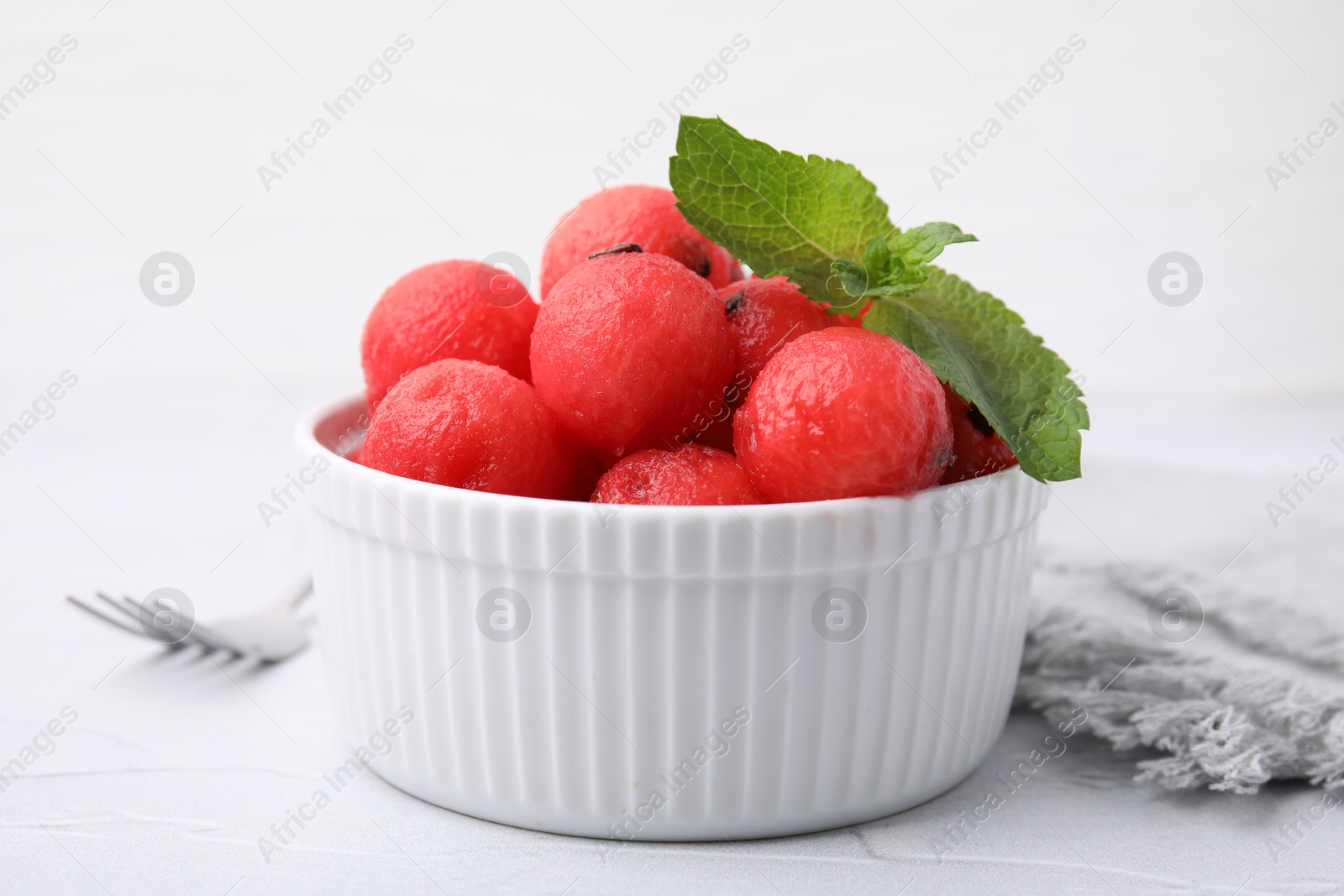 Photo of Tasty watermelon balls with mint in bowl on white table, closeup