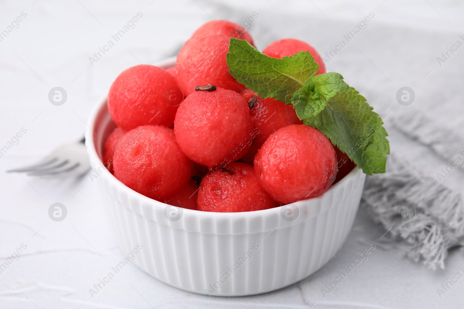 Photo of Tasty watermelon balls with mint in bowl on white table, closeup