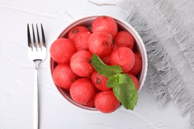 Photo of Tasty watermelon balls with mint in bowl served on white textured table, flat lay