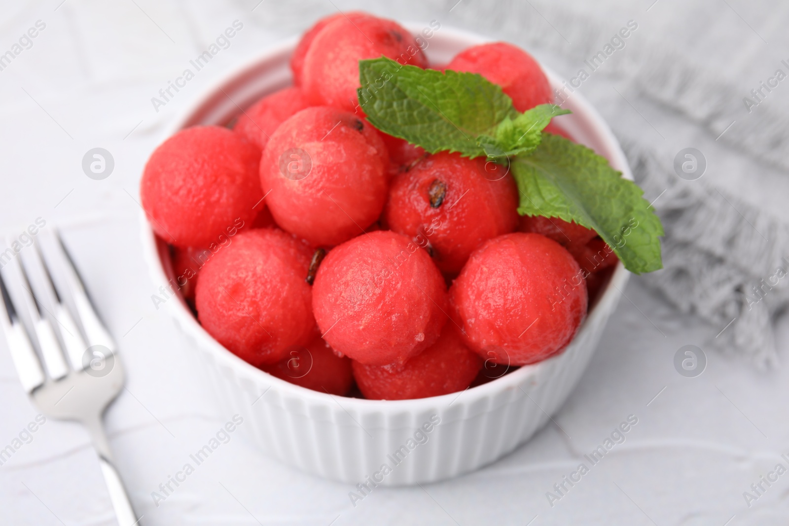 Photo of Tasty watermelon balls with mint in bowl served on white textured table, closeup