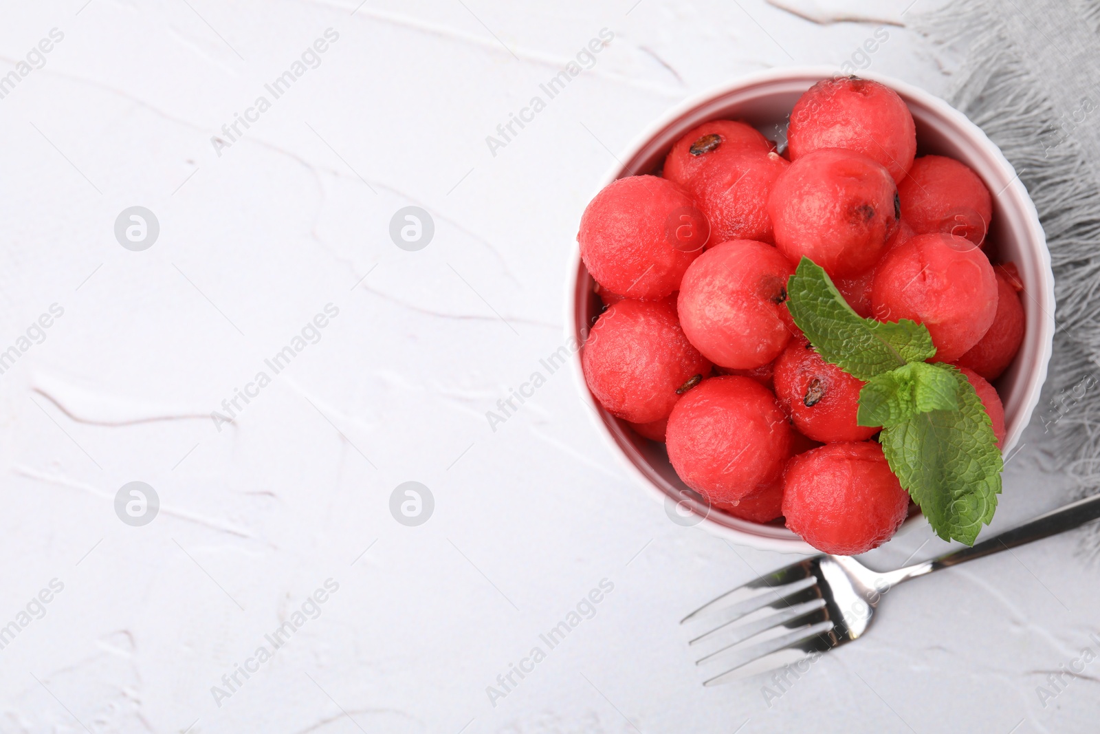 Photo of Tasty watermelon balls with mint in bowl served on white textured table, flat lay. Space for text