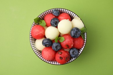 Photo of Tasty watermelon and melon balls with blueberries in bowl on green table, top view