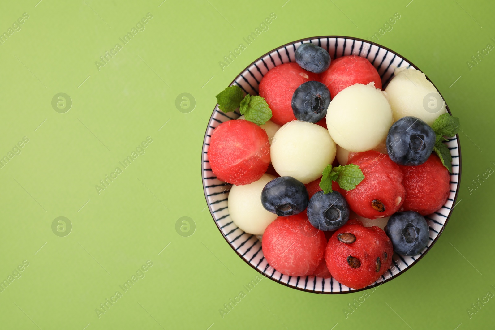 Photo of Tasty watermelon and melon balls with blueberries in bowl on green table, top view. Space for text