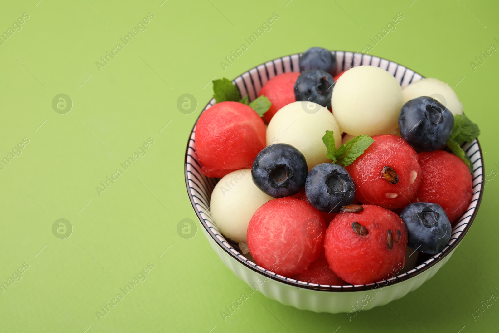 Photo of Tasty watermelon and melon balls with blueberries in bowl on green table, closeup. Space for text