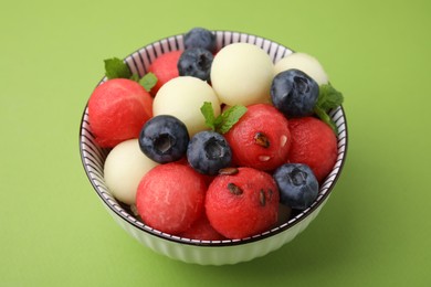 Photo of Tasty watermelon and melon balls with blueberries in bowl on green table, closeup