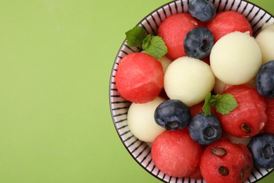 Photo of Tasty watermelon and melon balls with blueberries in bowl on green table, top view. Space for text