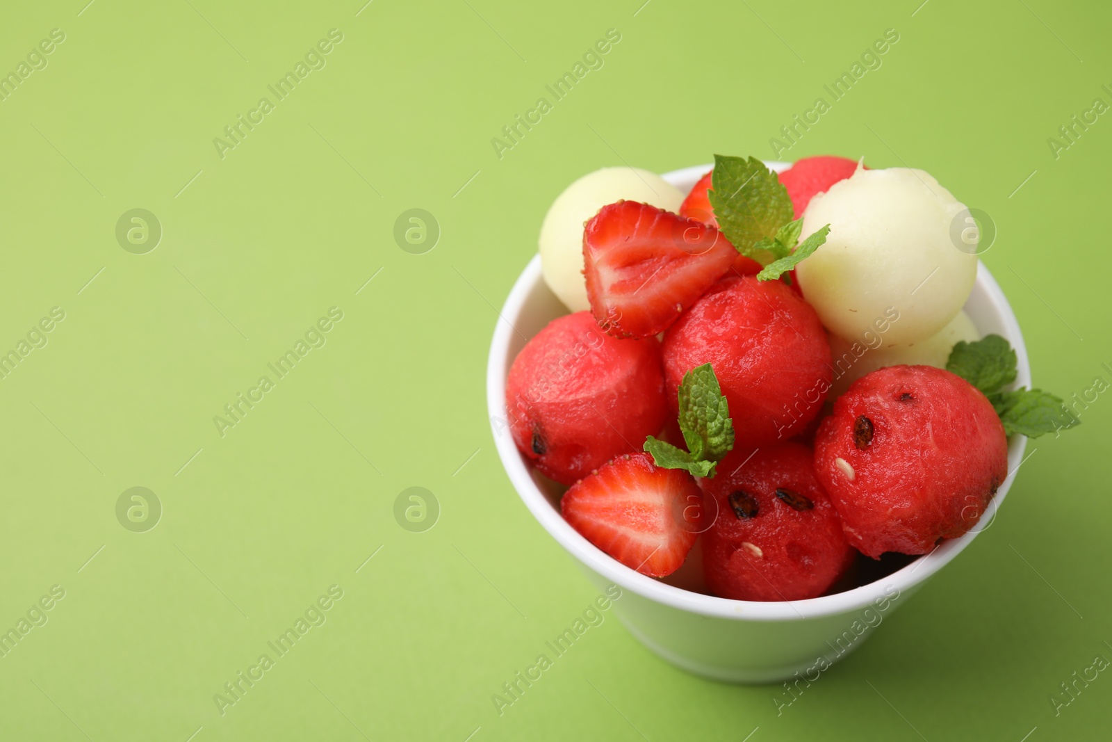 Photo of Tasty watermelon and melon balls with strawberries in bowl on green table, closeup. Space for text