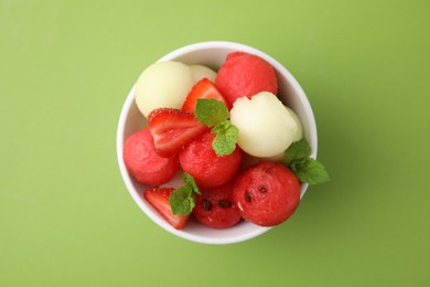 Photo of Tasty watermelon and melon balls with strawberries in bowl on green table, top view