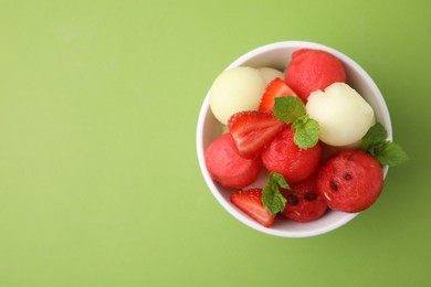 Tasty watermelon and melon balls with strawberries in bowl on green table, top view. Space for text