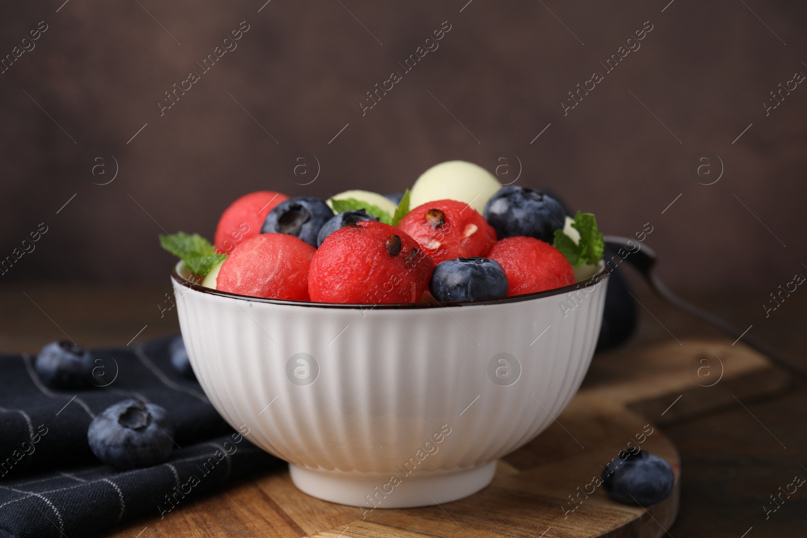 Photo of Tasty watermelon and melon balls with blueberries in bowl on table against brown background, closeup