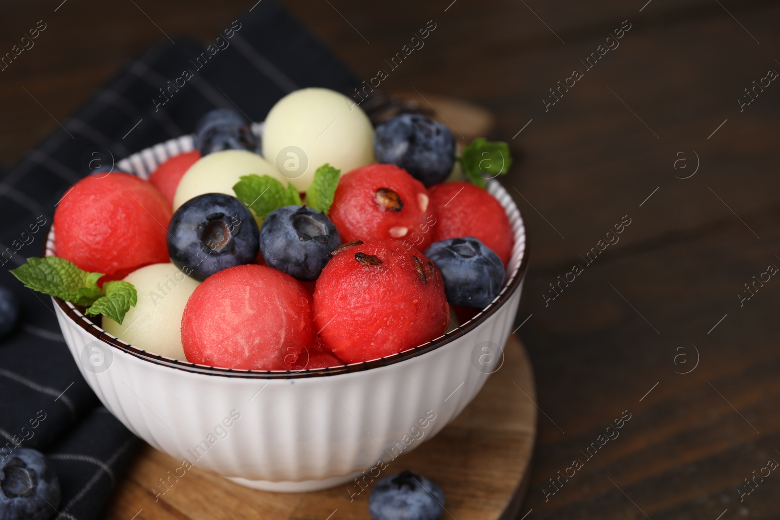 Photo of Tasty watermelon and melon balls with blueberries in bowl on wooden table, closeup