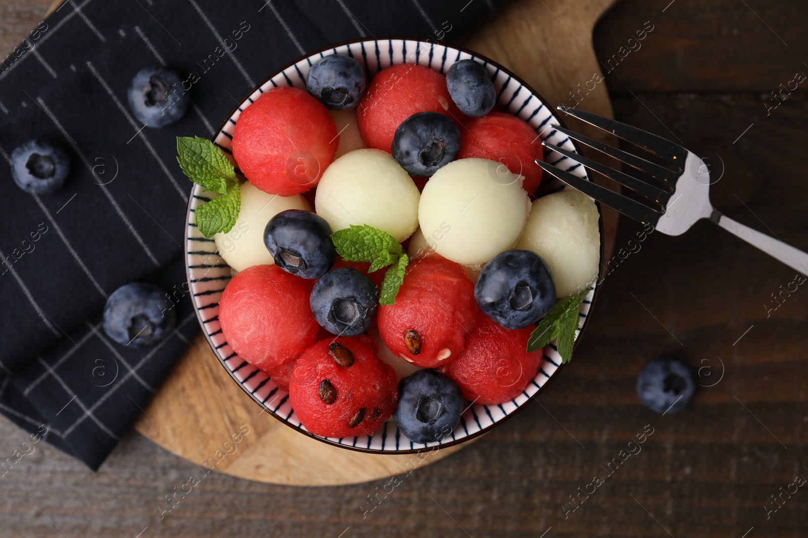 Photo of Tasty watermelon and melon balls with blueberries in bowl on wooden table, top view