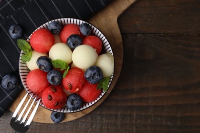 Photo of Tasty watermelon and melon balls with blueberries in bowl on wooden table, top view. Space for text