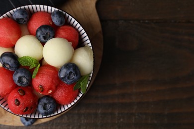 Photo of Tasty watermelon and melon balls with blueberries in bowl on wooden table, top view. Space for text