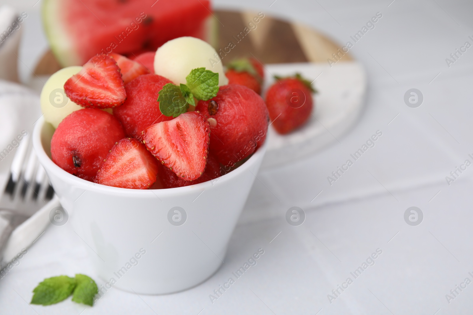 Photo of Tasty watermelon and melon balls with strawberries in bowl on white tiled table, closeup. Space for text