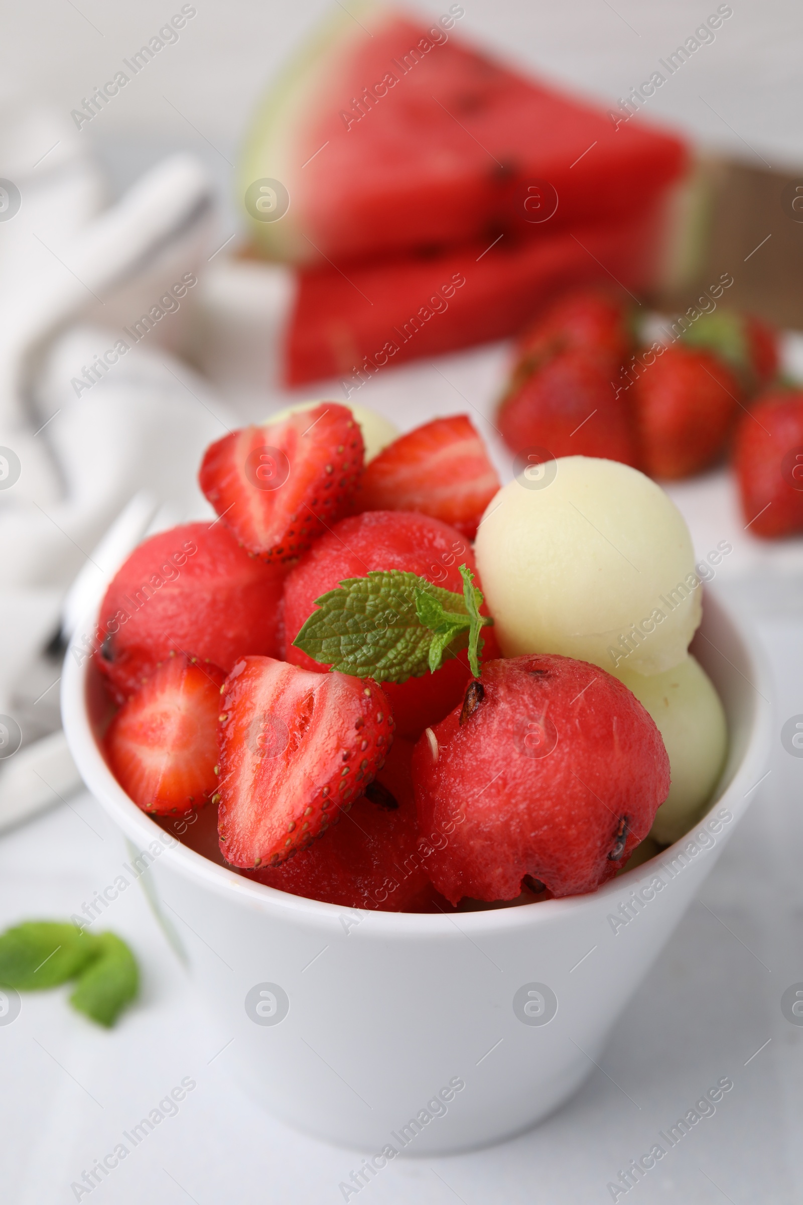 Photo of Tasty watermelon and melon balls with strawberries in bowl on white table, closeup