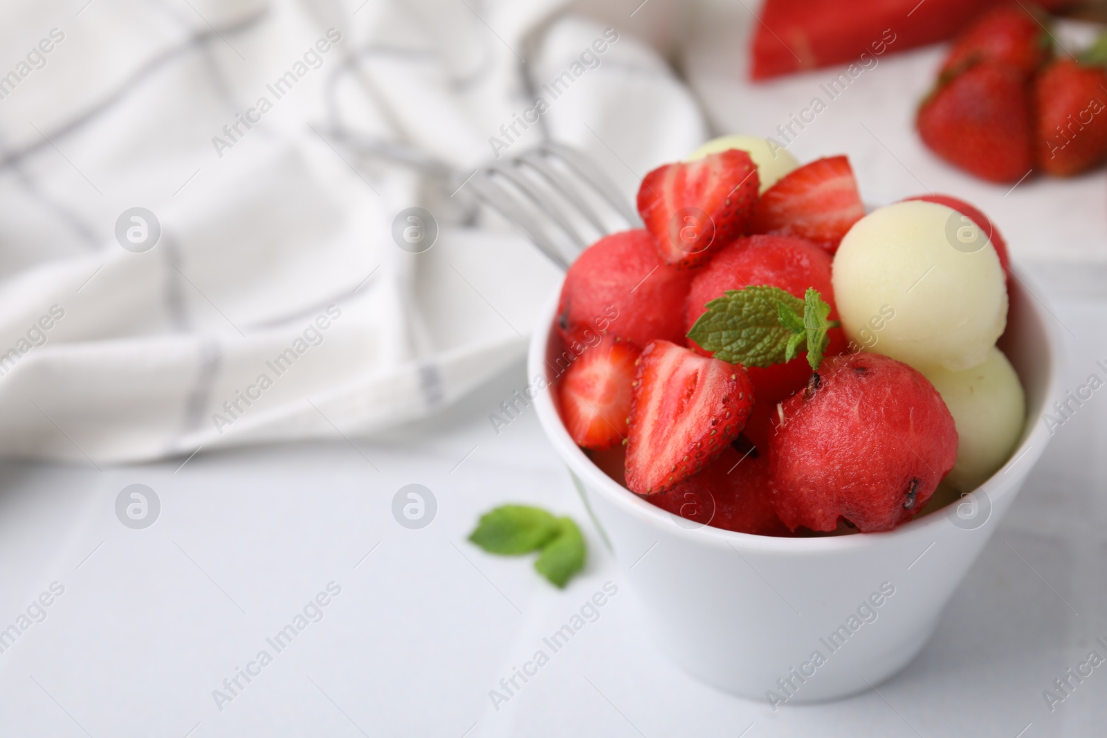 Photo of Tasty watermelon and melon balls with strawberries in bowl on white tiled table, closeup. Space for text