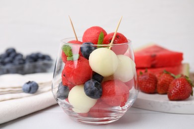 Photo of Tasty watermelon and melon balls with blueberries in glass on white table, closeup