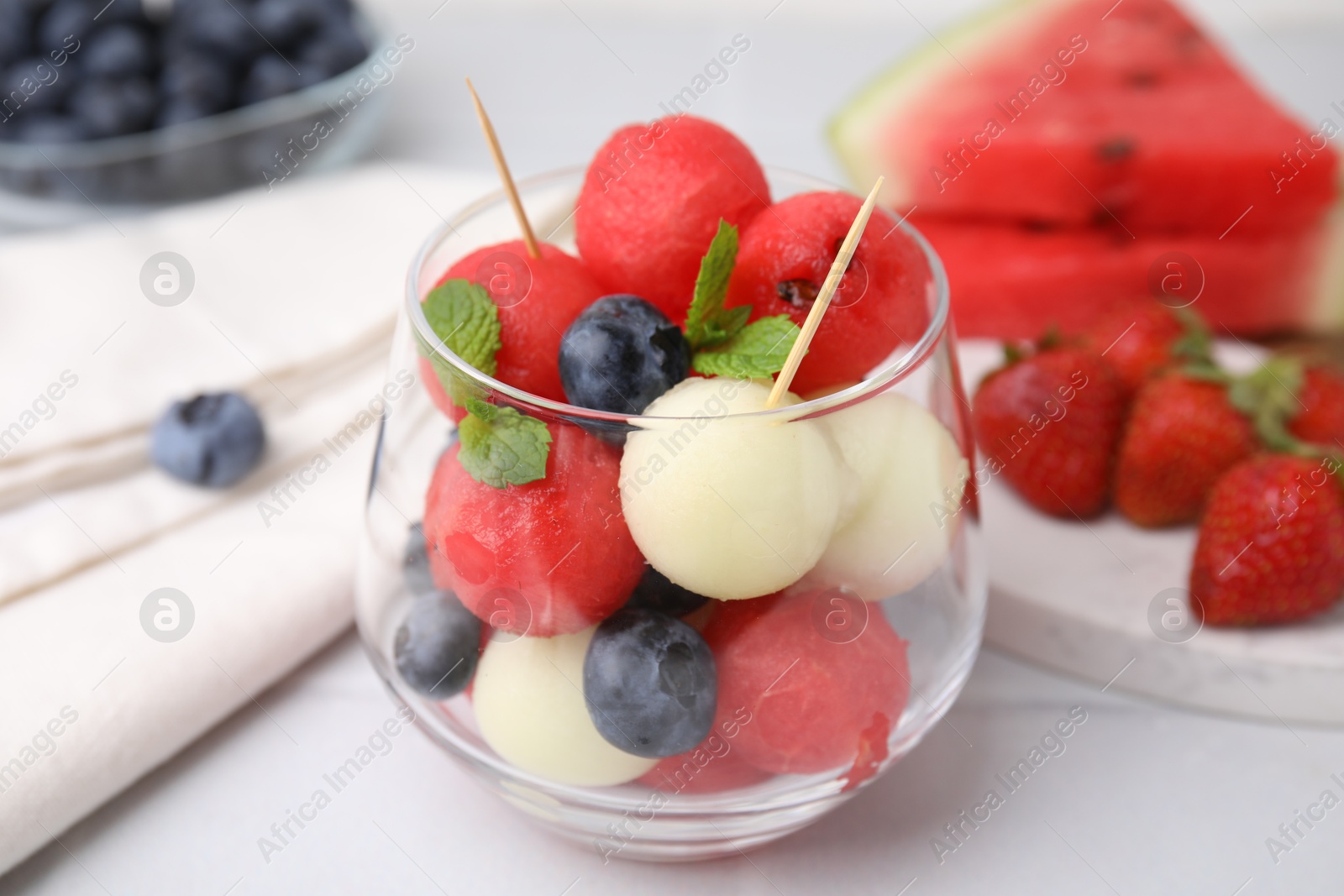 Photo of Tasty watermelon and melon balls with blueberries in glass on white table, closeup