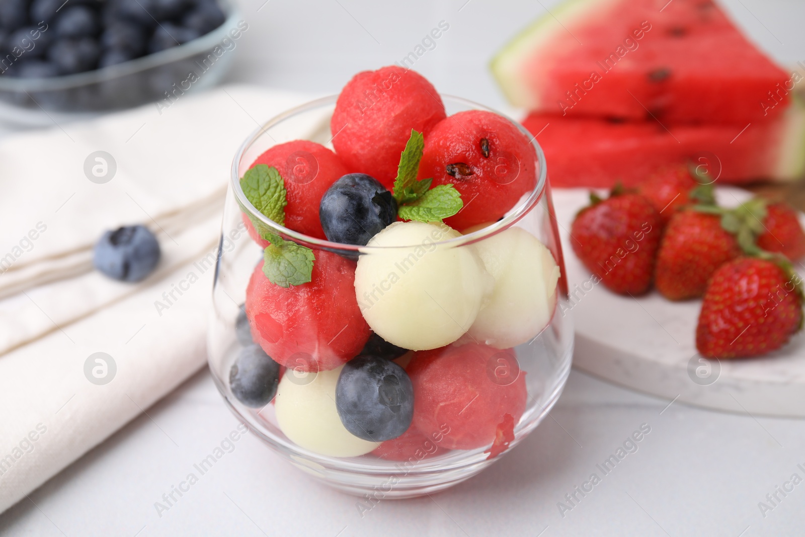 Photo of Tasty watermelon and melon balls with blueberries in glass on white table, closeup