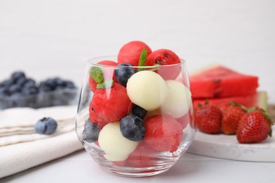 Photo of Tasty watermelon and melon balls with blueberries in glass on white table, closeup